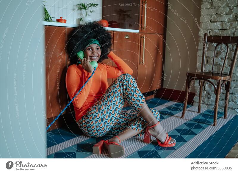 Retro housewife chatting on phone in colorful 50s kitchen woman afro rotary floor sitting 1950s retro vintage vibrant orange patterned pants cheerful