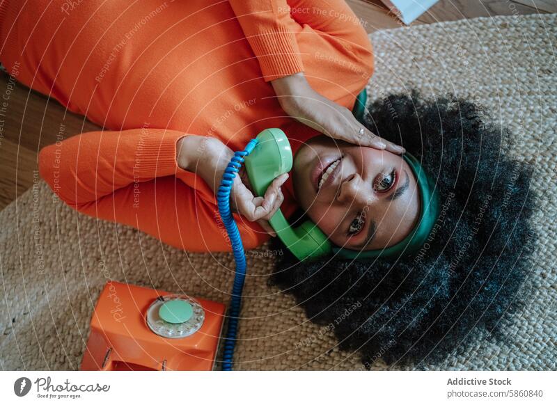 Woman in Orange Turtleneck Talking on Vintage Telephone woman black orange floor chatting rotary telephone playful carpet communication vintage colorful