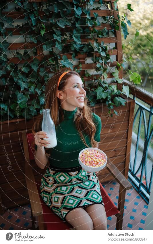 Retro inspired woman enjoying cereal and milk on balcony retro 1950s fashion ivy green dress sitting looking away smiling colorful breakfast vintage foliage