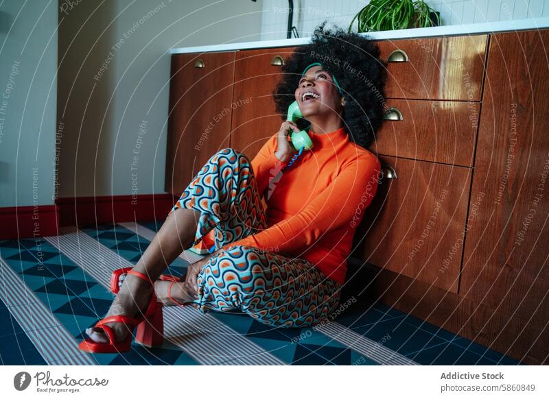 Retro housewife chatting on phone in colorful 50s kitchen woman afro rotary floor sitting 1950s retro vintage vibrant orange patterned pants cheerful