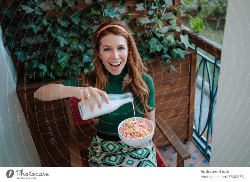 Cheerful woman in 50s attire pouring milk into cereal on a balcony redhead 1950s breakfast vintage retro housewife fashion style joy happy smile porch ivy green