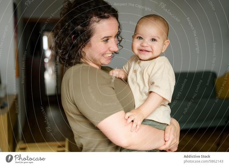 Happy mother holding her smiling toddler at home smile laughing family parent child indoor living room happy joy bonding care love mom boy girl playful cheerful