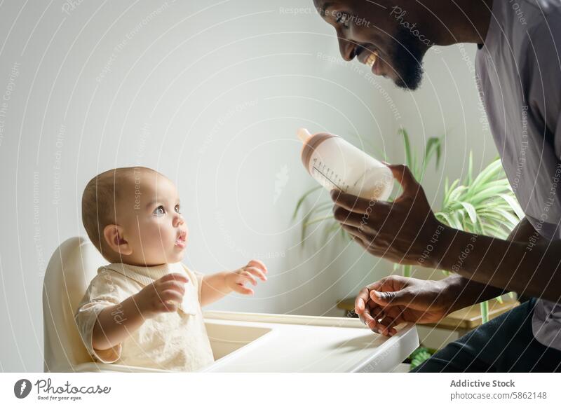 African American father feeding his baby with a bottle highchair african american child parent nutrition feeding time infant family care bonding interaction