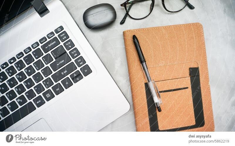 There is a work desk with a laptop, notebook, glasses and earbuds. Desk Notebook