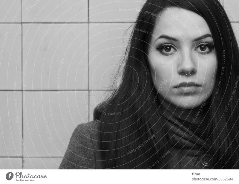 Woman with coat and scarf Feminine Piercing Dark-haired Long-haired Meditative Looking Observe look Scarf Coat wall tiles Looking into the camera