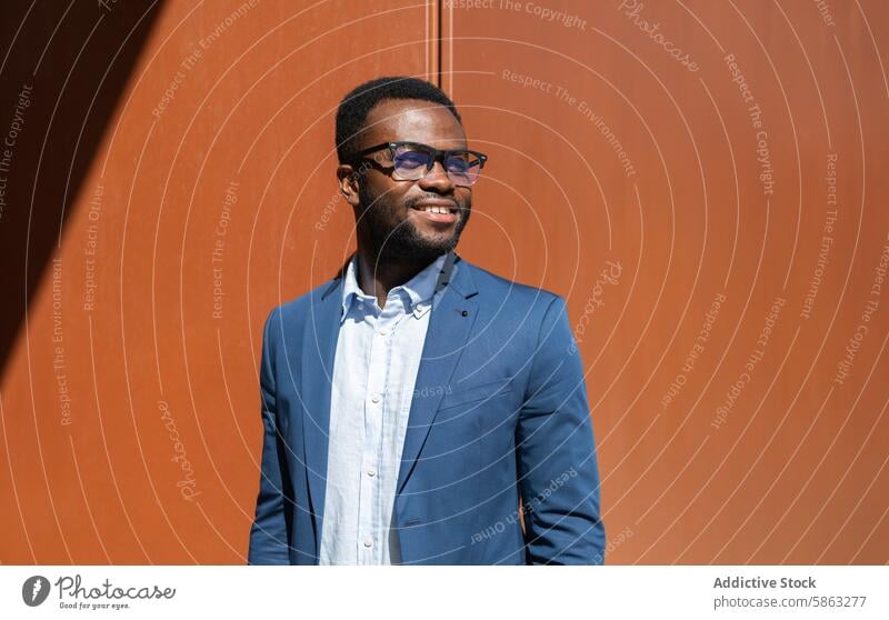 Smiling African American businessman in blue suit outdoors african american glasses smiling orange wall side look professional relaxed inviting sunny corporate