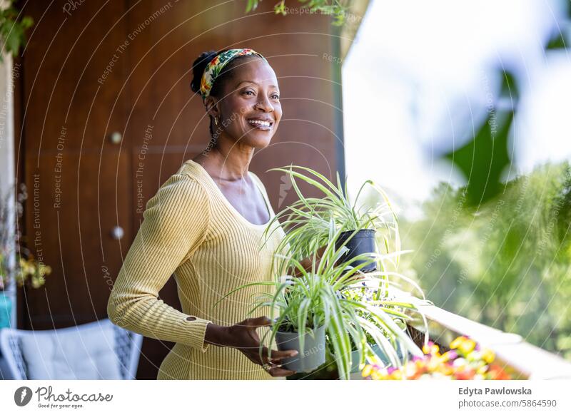 Smiling woman holding potted plants on the balcony at home people joy black natural attractive black woman happiness happy real people mature adult daily life