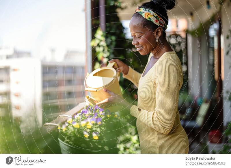 Beautiful woman watering plants on the balcony people joy black natural attractive black woman happiness happy real people mature adult daily life one person