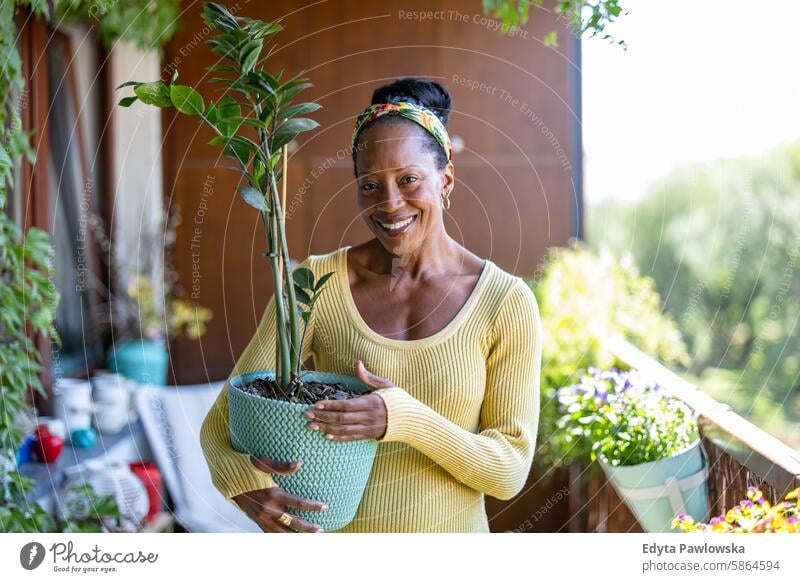 Smiling woman holding potted plants on the balcony at home people joy black natural attractive black woman happiness happy real people mature adult daily life