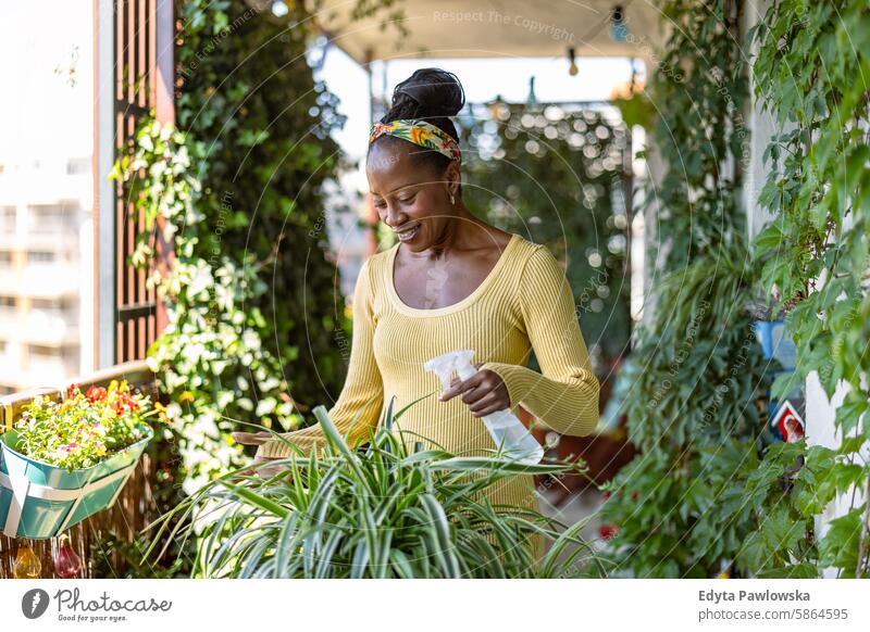 Beautiful woman watering plants on the balcony people joy black natural attractive black woman happiness happy real people mature adult daily life one person