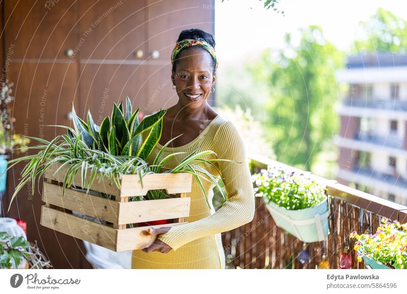 Smiling woman holding potted plants on the balcony at home people joy black natural attractive black woman happiness happy real people mature adult daily life