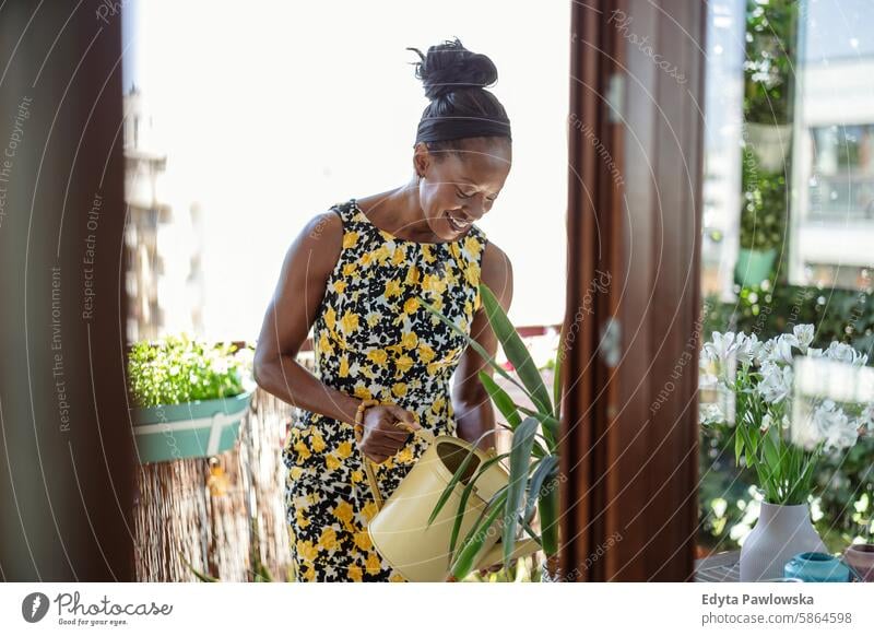 Beautiful woman watering plants on the balcony people joy black natural attractive black woman happiness happy real people mature adult daily life one person