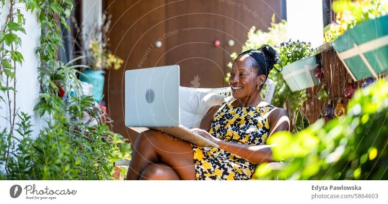 Smiling woman using laptop while sitting on the balcony people joy black natural attractive black woman happiness happy real people mature adult daily life