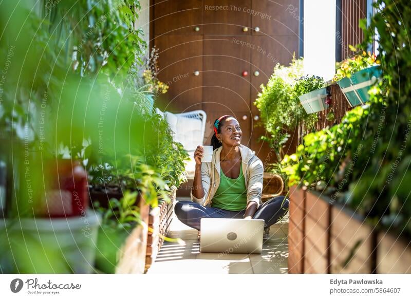 Smiling woman using laptop while sitting on the balcony people joy black natural attractive black woman happiness happy real people mature adult daily life