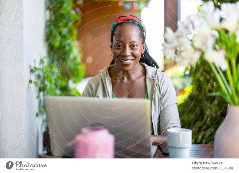 Smiling woman using laptop while sitting on the balcony people joy black natural attractive black woman happiness happy real people mature adult daily life