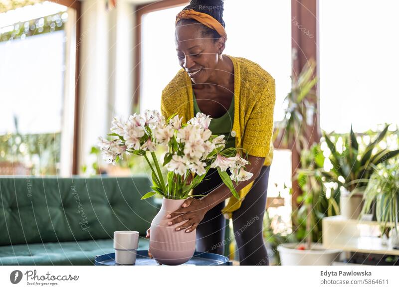 Portrait of smiling woman holding vase with flowers at home people joy black natural attractive black woman happiness happy real people mature adult daily life