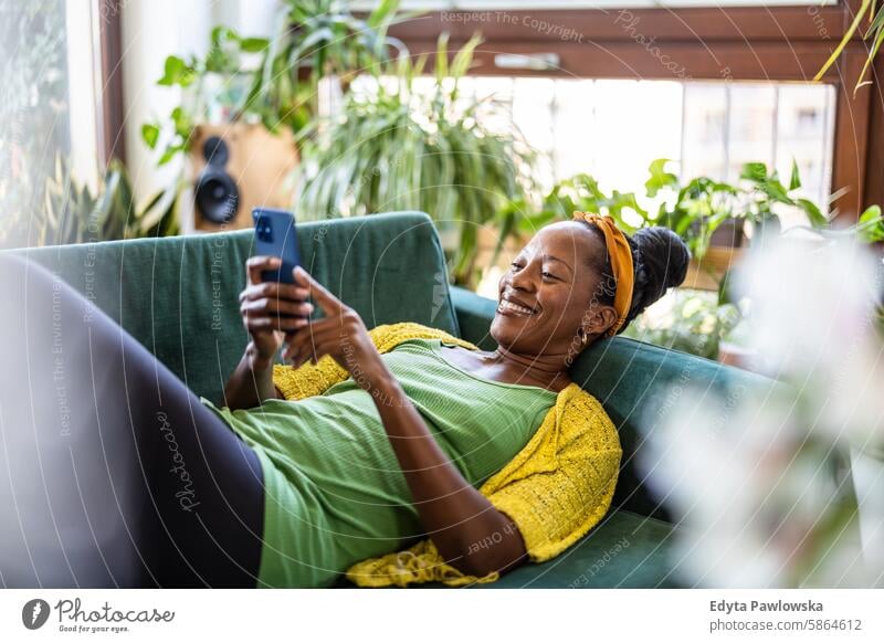 Woman using smartphone while relaxing on sofa at home people joy woman black natural attractive black woman happiness happy real people mature adult daily life