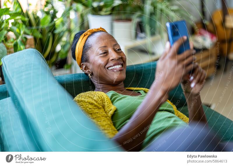 Woman using smartphone while relaxing on sofa at home people joy woman black natural attractive black woman happiness happy real people mature adult daily life