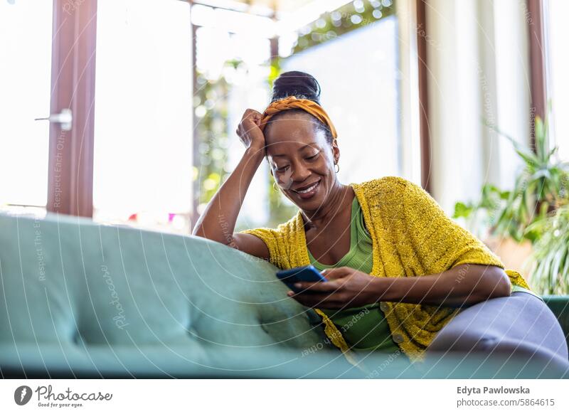 Woman using smartphone while relaxing on sofa at home people joy woman black natural attractive black woman happiness happy real people mature adult daily life