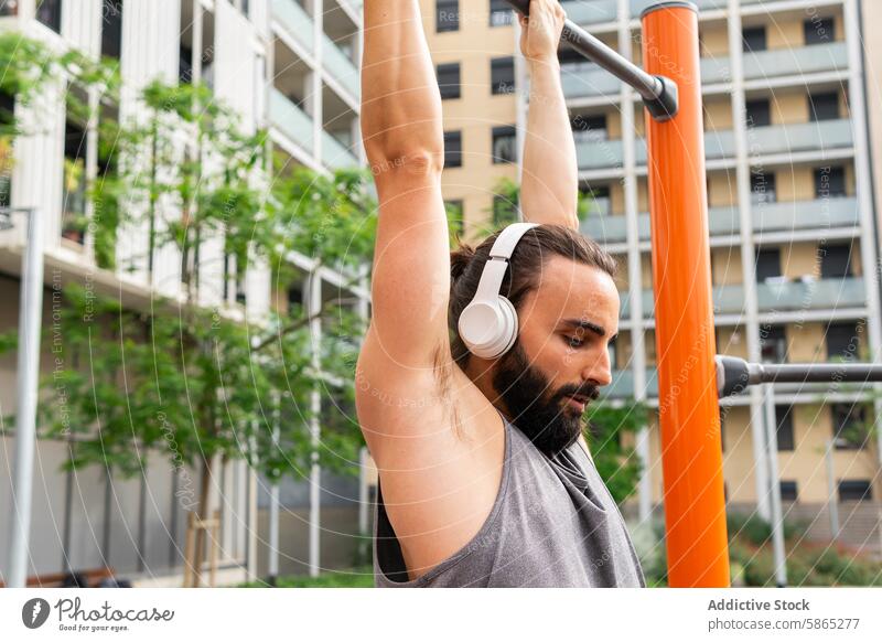 Young man works out at outdoor gym in Poblenou young workout poblenou urban park beard headphones exercise fitness sport lifestyle casual attire summer day city