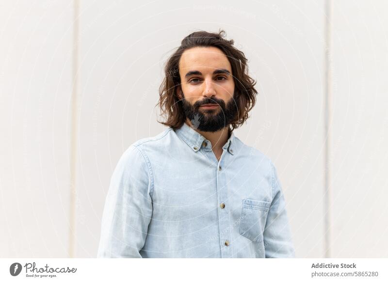 Confident man in casual attire standing against a plain background portrait confident relaxed urban modern lifestyle denim shirt blue long hair beard young male