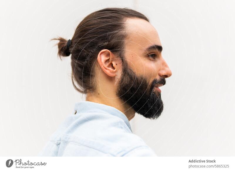 Profile view of a bearded young man against a plain background profile adult male ponytail casual shirt light blue neat hairstyle facial hair fashion head side