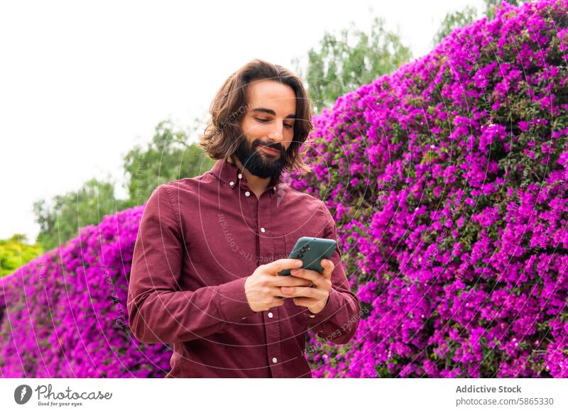 Man using smartphone in vibrant Poblenou park man poblenou purple flower lifestyle outdoor browsing technology mobile connectivity internet social media leisure