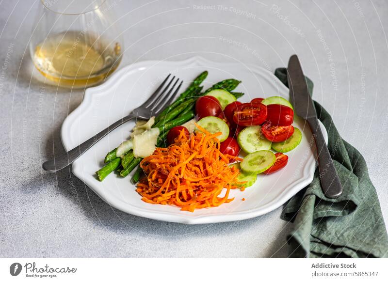 Fresh vegetable salad with asparagus and grated carrot cheese tomato cucumber plate healthy meal fresh dressing cutlery white halved cherry slices raw organic