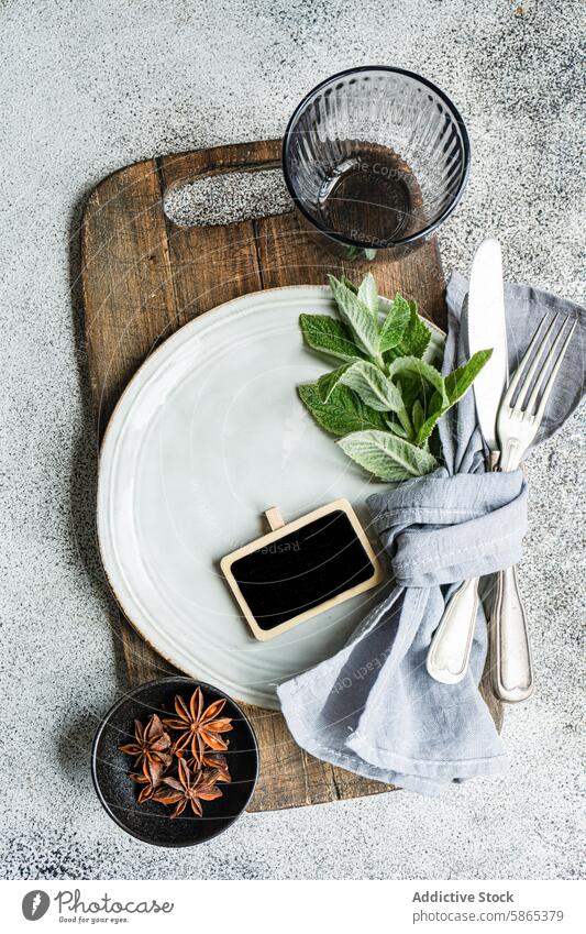 Elegant summer table setting with a fresh mint theme white plate gray napkin silver utensil fork knife wooden board blackboard glass cup anise star spice