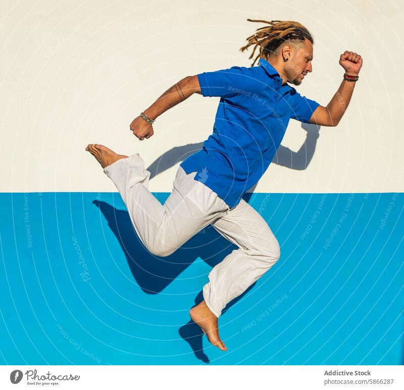 Man with dreadlocks performing street dance on blue background dancer man dynamic movement action performance mid-air street art urban contemporary style