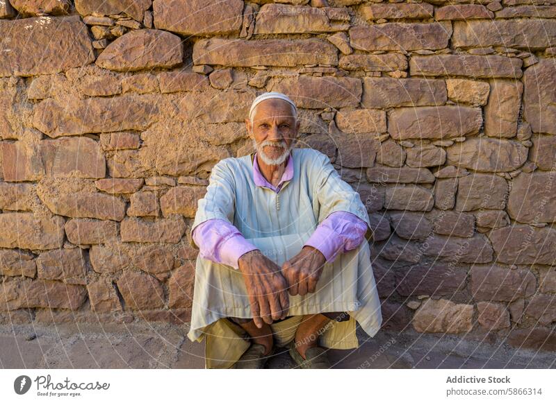 Elderly Moroccan man seated against a stone wall in traditional attire elder moroccan cultural heritage history morocco north africa clothes traditional dress