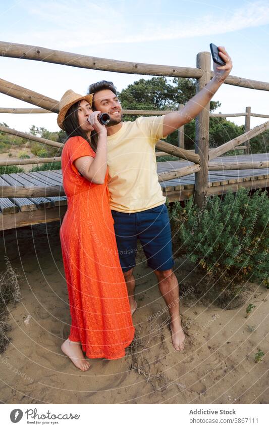 Couple taking selfie and enjoying beers outdoors couple summer casual barefoot bright attire man woman drinking enjoyment leisure technology mobile phone