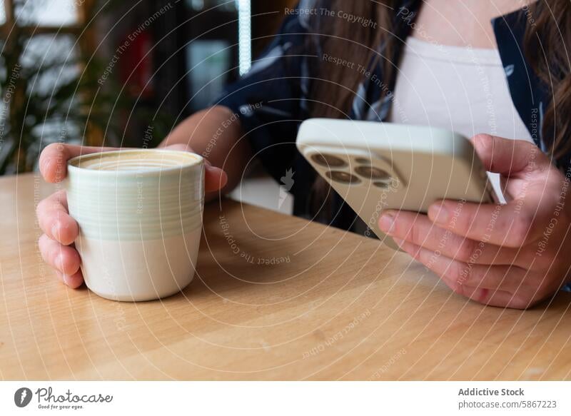 Cropped unrecognizable woman with coffee and smartphone at a table hand cup wood gadget device mobile phone anonymous faceless cropped hold beverage technology