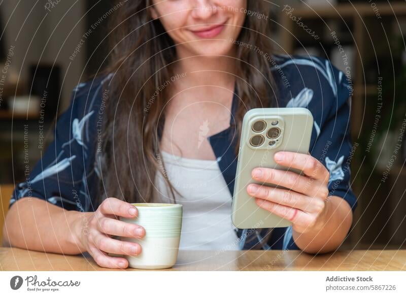 Woman enjoys coffee while browsing smartphone at home woman casual smile drink technology mobile phone gadget device looking down cup hand table relaxation