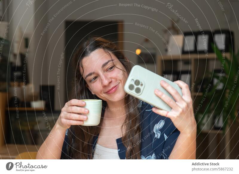 Woman enjoys coffee while taking a selfie with smartphone woman coffee break camera smiling drink technology gadget mobile phone casual moment relaxation happy