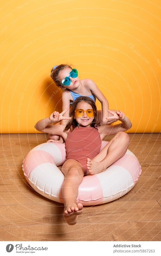 Two children posing in summer-themed studio setup pose playful yellow background outfit sunglasses colorful inflatable ring girl boy fun joy happy peace sign