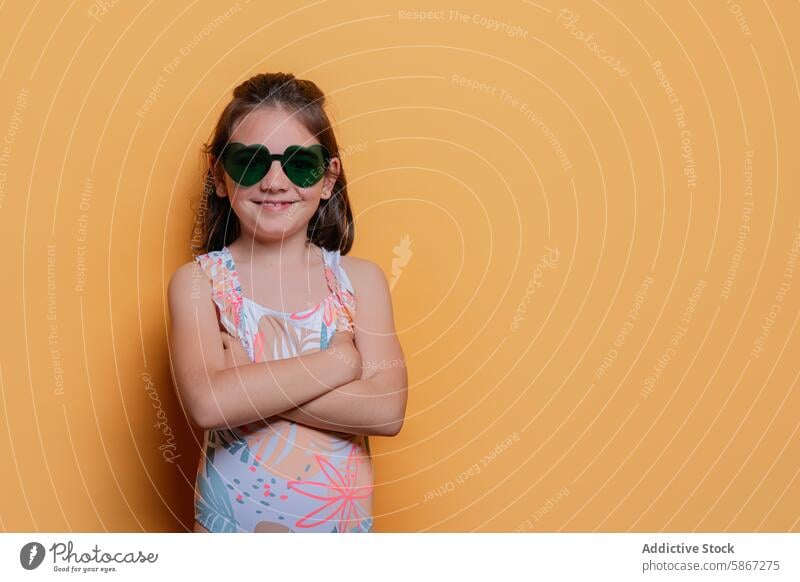 Young girl in swimwear and sunglasses against yellow background child summer studio posing confident arms crossed vibrant fun cheerful floral fashion apparel