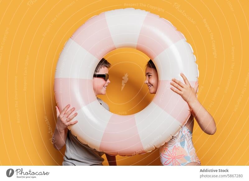 Two children playing with a swim ring in summer theme setup fun joy yellow background studio boy girl playful happiness bright color leisure vacation swimwear