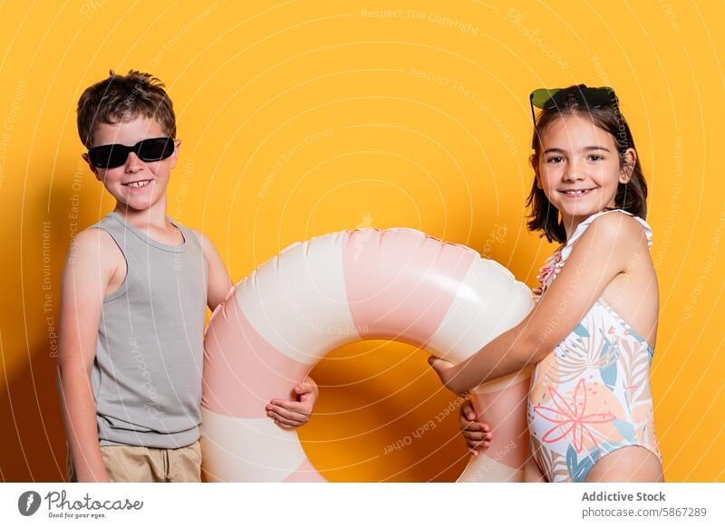 Summer fun with stylish children in a vibrant studio setting summer theme boy girl sunglasses swimsuit lifering playful pose bright color fashion style leisure