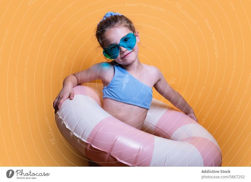 Young girl with summer props in studio setting inflatable float sunglasses playful orange background child youthful fashion casual fun bright colorful leisure