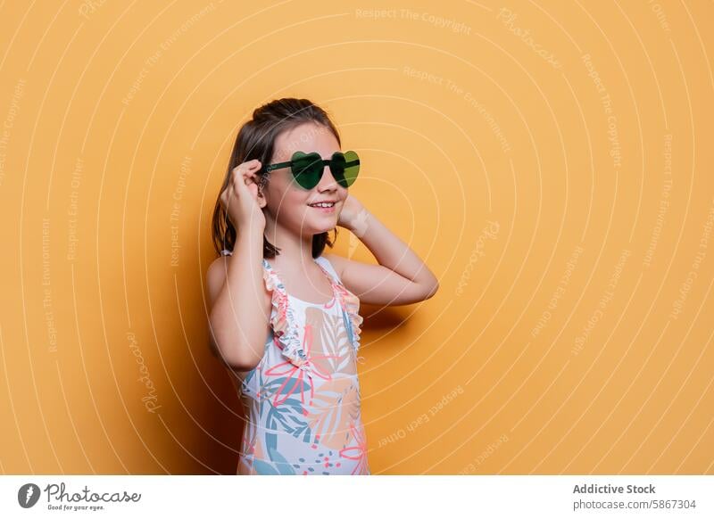 Young girl in sunglasses and swimwear against yellow background child summer studio cheerful young vibrant theme pose fashion style accessory youth playful joy