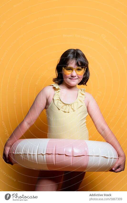 Child posing with swim ring in summer studio setup child heart-shaped sunglasses swimsuit orange backdrop yellow pink girl fun vibrant portrait photography