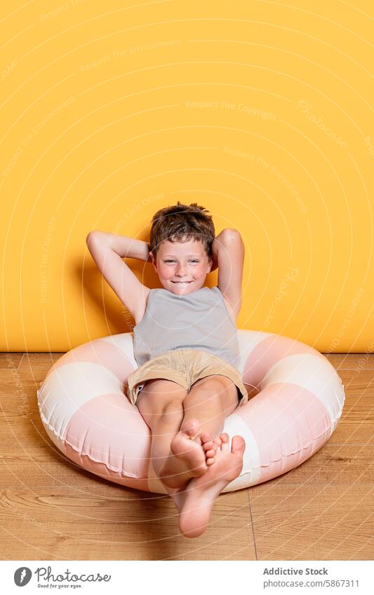 Young boy enjoying summer vibes in a studio setting child theme inflatable fun indoor yellow backdrop cheerful lounging essence playful happiness leisure