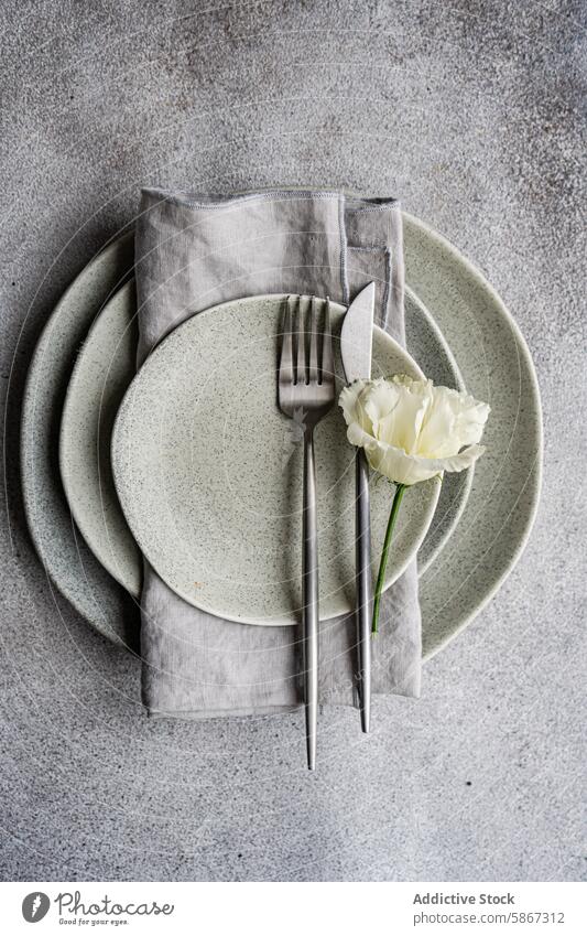 From above of elegant Godetia flower on a stylish plate and cutlery set table setting godetia ceramic napkin linen sleek delicate texture gray background fork