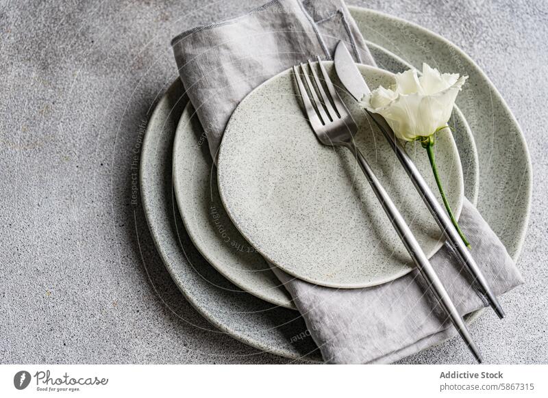 Elegant table setting with godetia flower and rustic tableware ceramic plate speckled silver cutlery fork knife linen napkin elegant modern textured surface