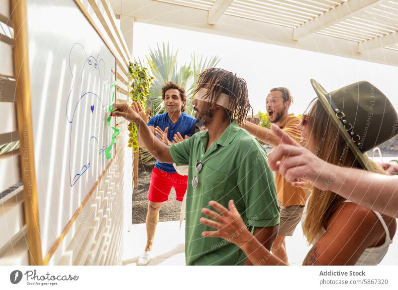 Friends playing a blindfolded drawing game during a party summertime friends outdoor excitement laughter cheering hints festive group casual leisure recreation