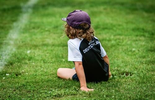 A boy in a soccer jersey takes a break on the pitch Boy (child) Meadow Lawn Child Foot ball Football pitch UEFA European Championship EM2024 Cap Green Sports