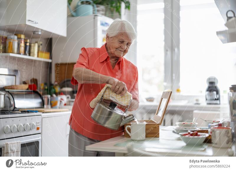 Senior woman pouring water into teapot at home kitchen enjoying contented people senior mature female elderly house old aging domestic life grandmother