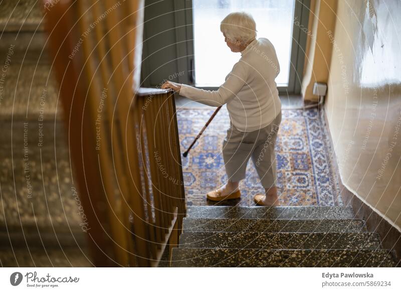 Elderly woman walking down the stairs leaning on a wooden cane people senior mature female elderly home house old aging domestic life grandmother pensioner