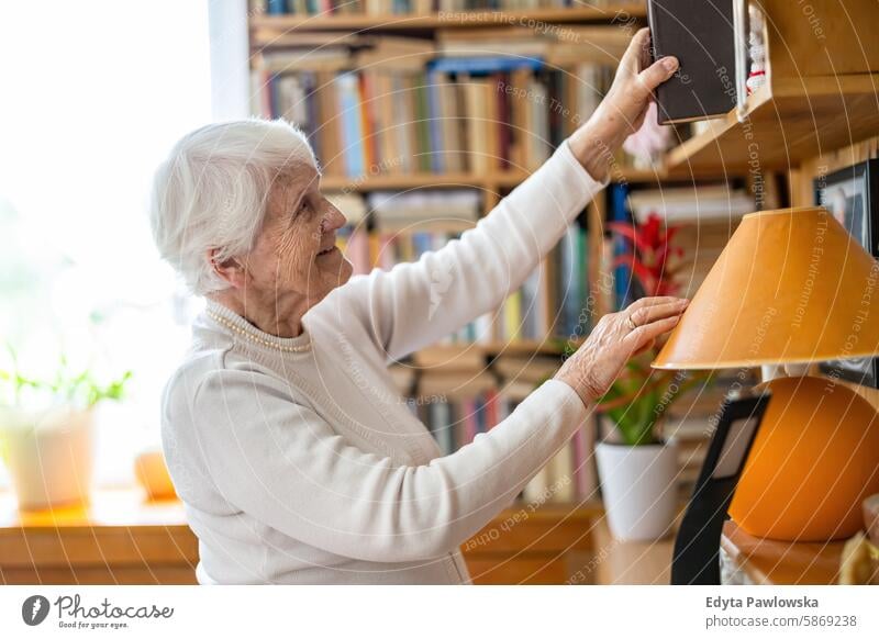 Senior woman selecting book from bookshelf at home smiling happy enjoying positive contented people senior mature female elderly house old aging domestic life